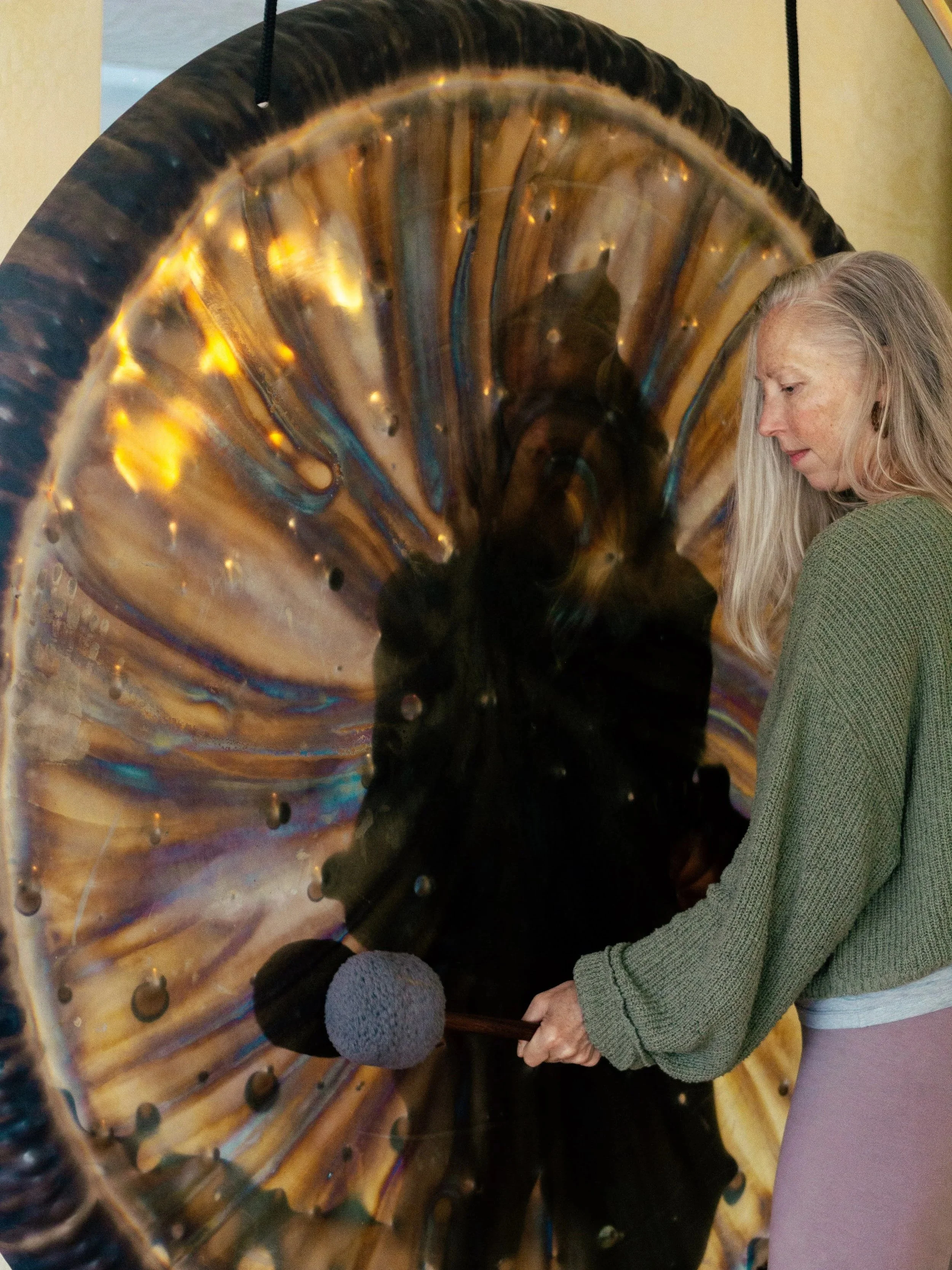 Blonde woman playing large gold, silver, and blue ish gond with gray fuzzy mallet.
