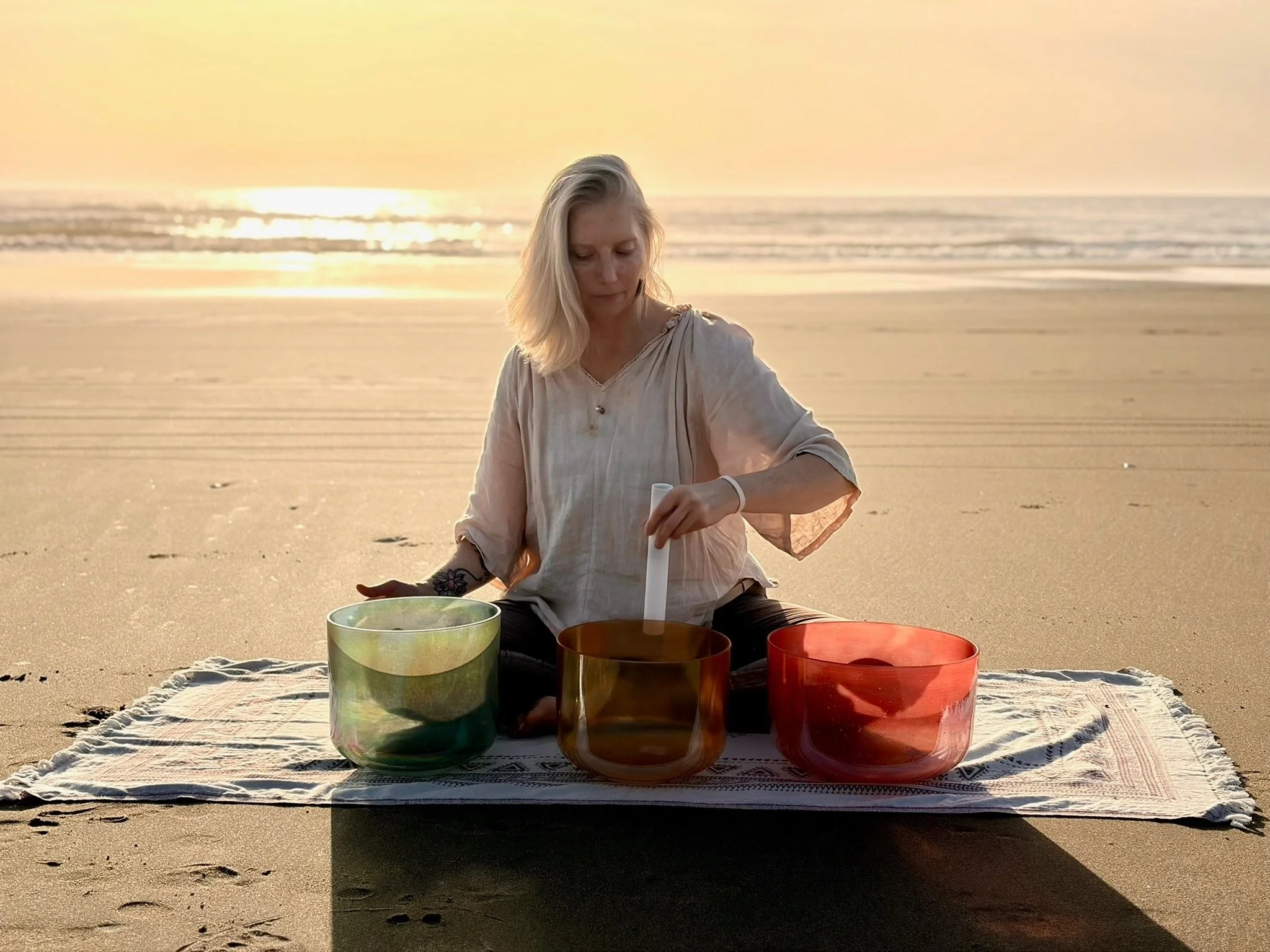 Woman with bolnde hair playing crystal boawls on the beach at sunset.