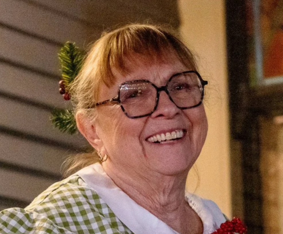 Smiling older woman wearing glasses and a plaid shirt.