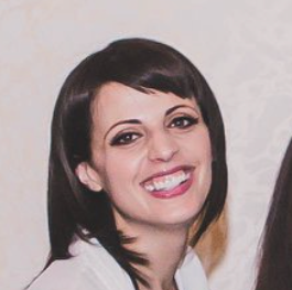 Smiling woman with dark hair wearing a white top against a light background
