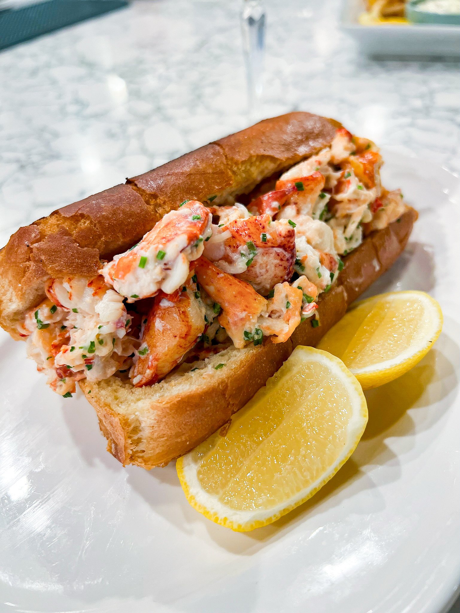 Lobster roll with lemon wedges on a white plate.