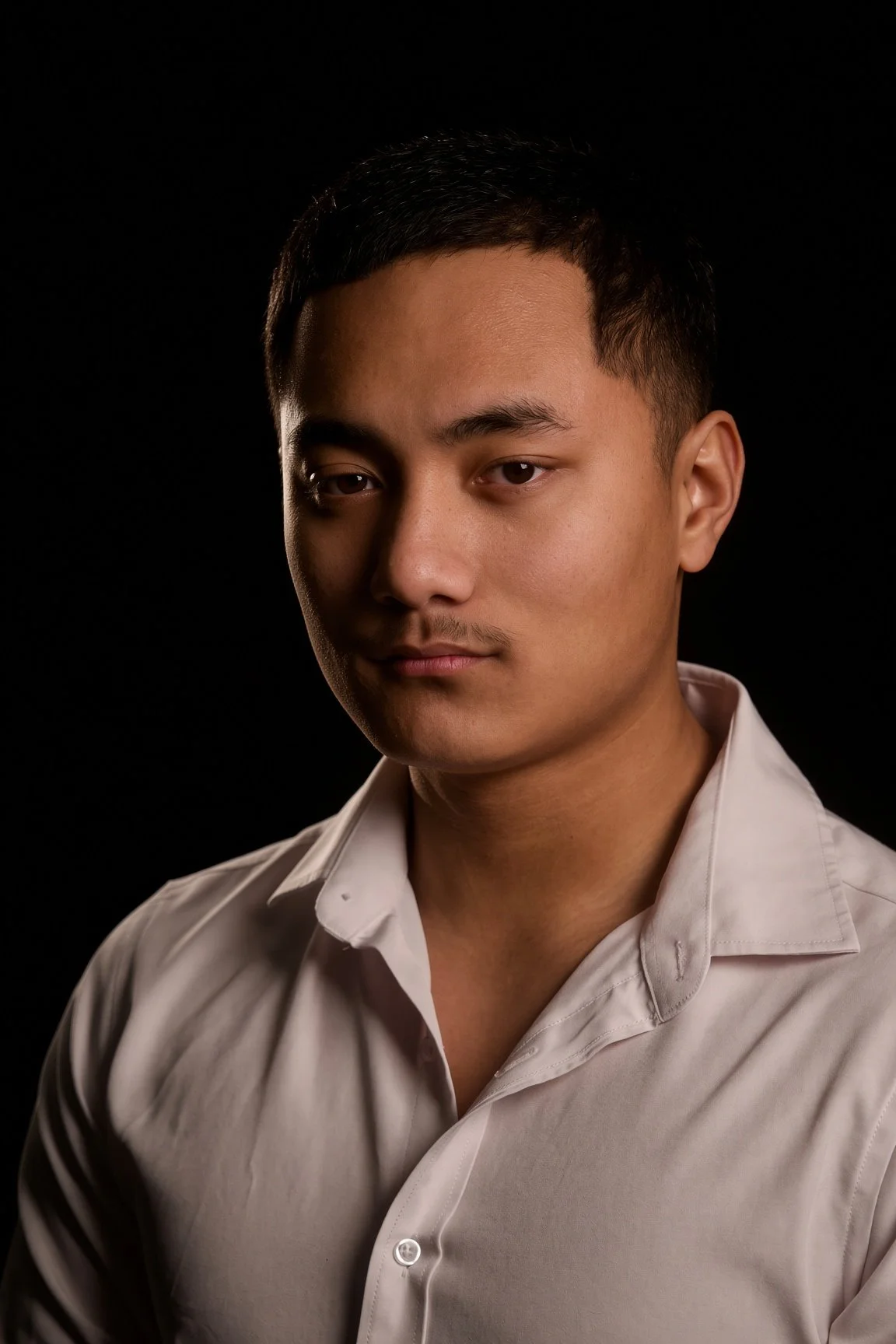 Portrait of a young Asian man with short black hair, wearing a white dress shirt, set against a dark background.