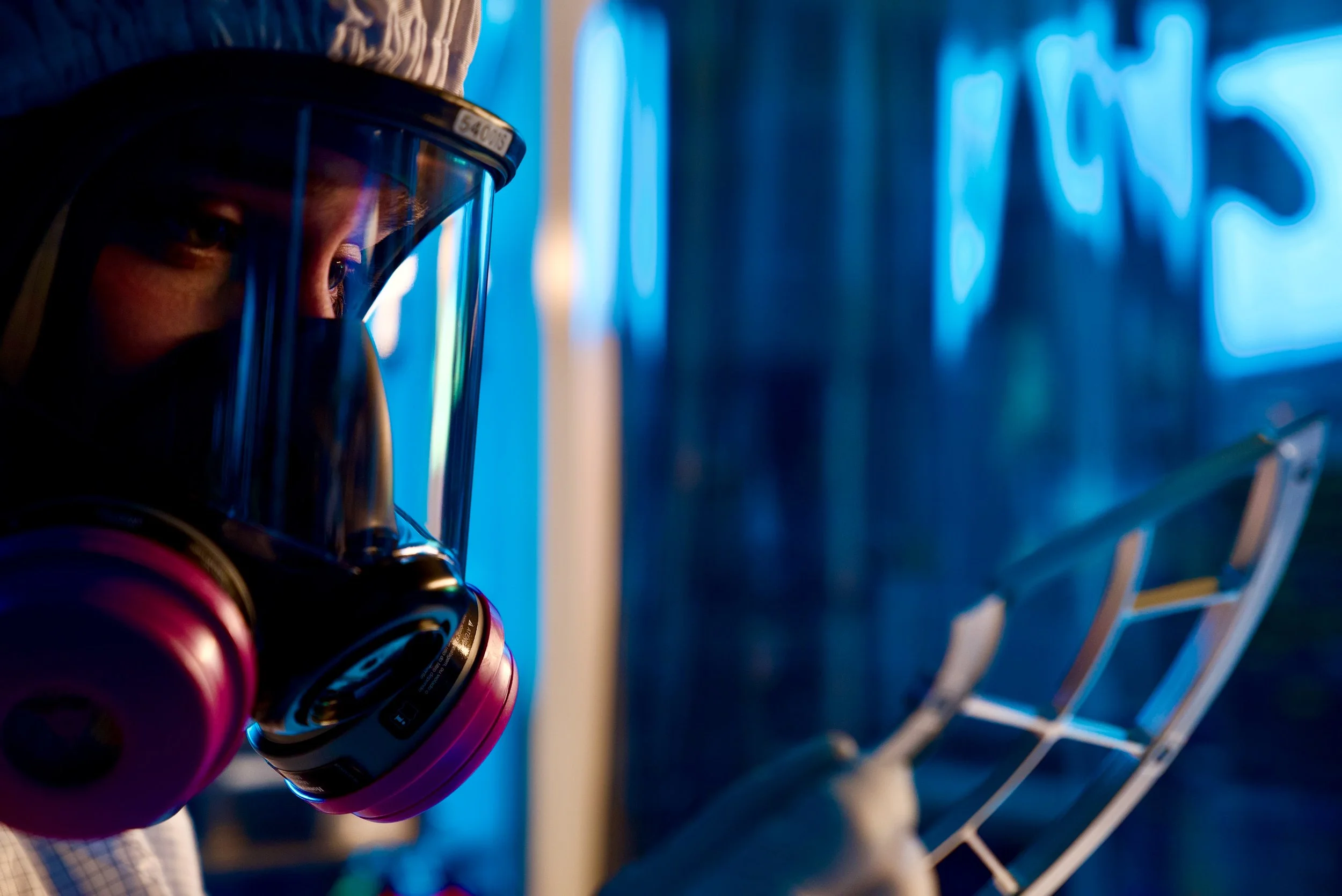 Close-up of a person wearing a face shield and pink gloves, reaching into a fridge for a bottle.