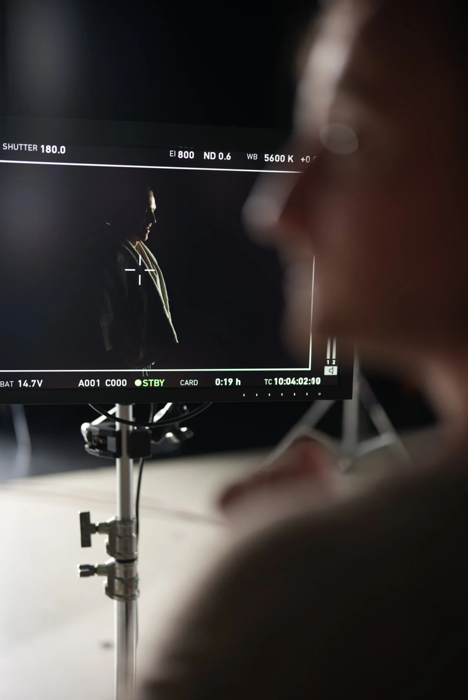 A person on set is looking at a monitor showing a silhouette of a woman with a dark background.