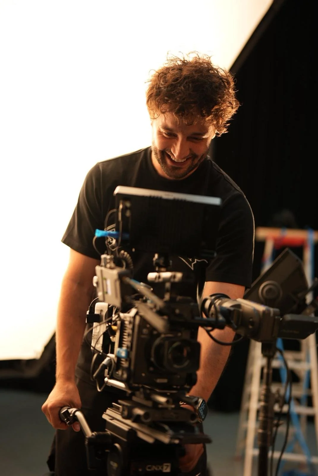 Man smiling while operating a professional video camera on a film set.