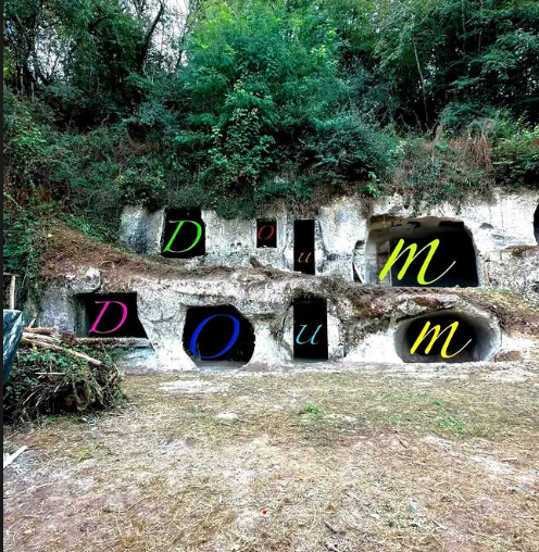 photo of hillside with trees and cave openings with the letters "D" "O" "U" "M" placed over the multiple cave openings