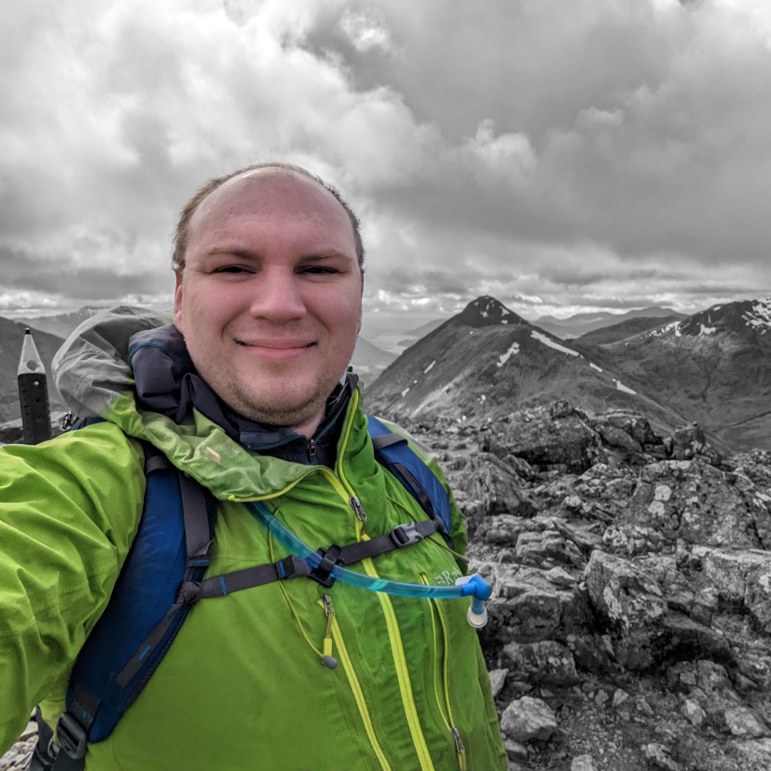  Spencer in a bright green raincoat taking a selfie on top of a rocky mountain 