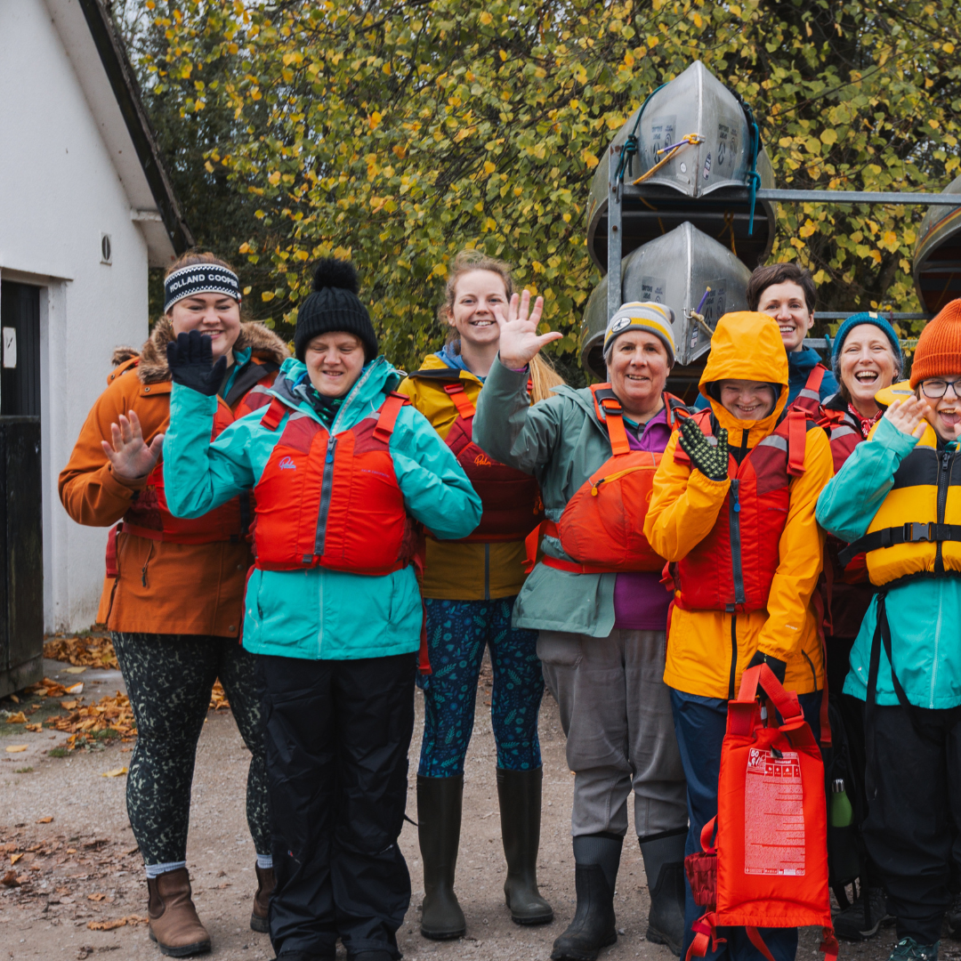  Group photo from organised day of water sports. Everyone is wearing life jackets and smiling/waving at camera  