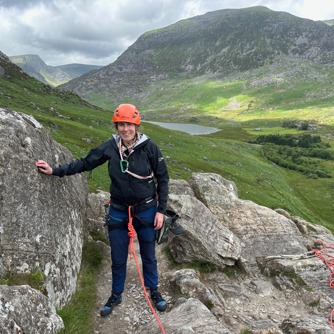  Emma out in the mountains with climbing gear on them and a rope attached to their harness.  