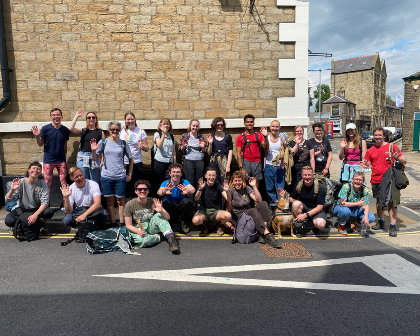  Large group smiling and waving stood in front of a brick wall 