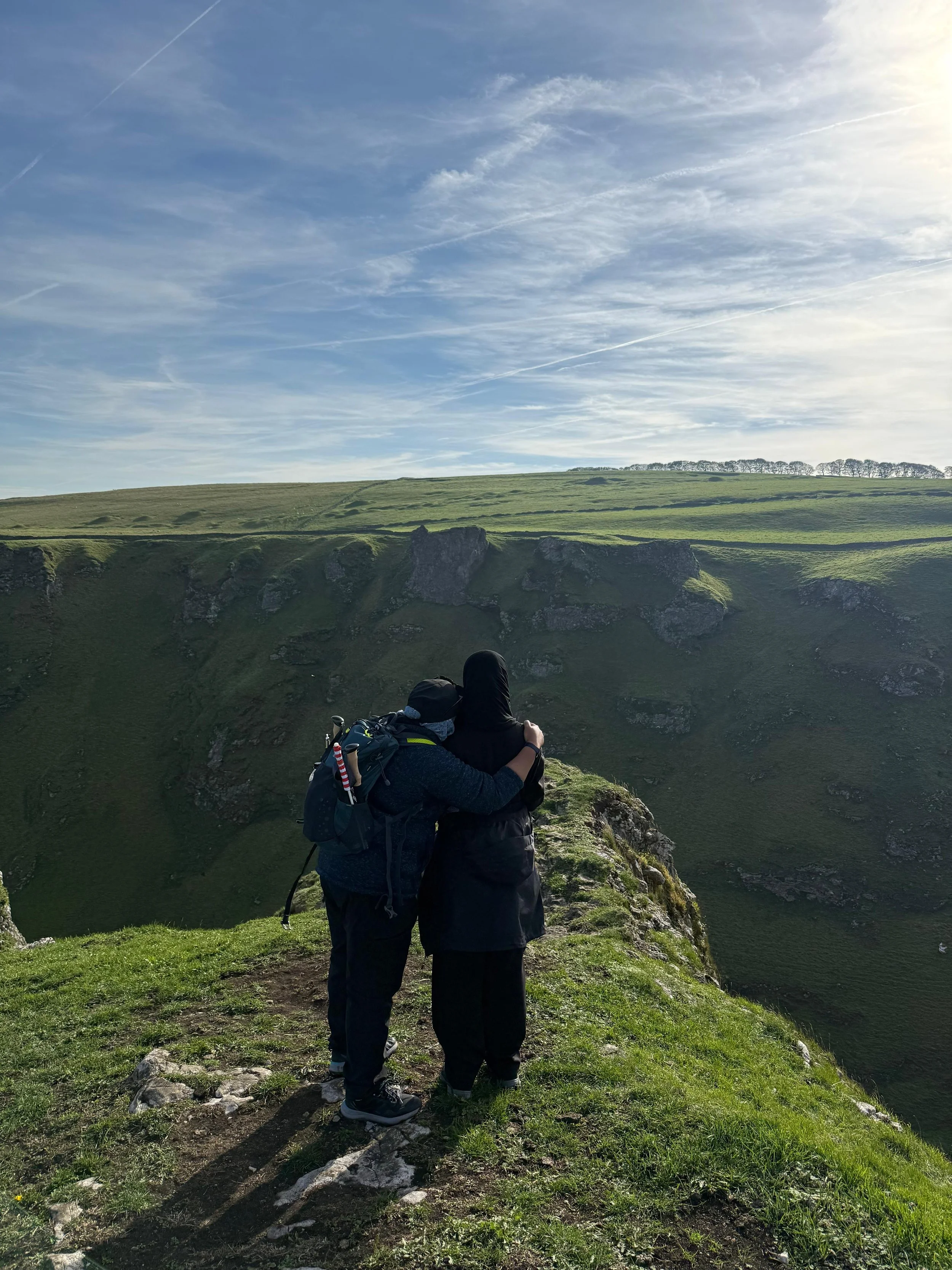 Two people hugging on a hill looking outwards