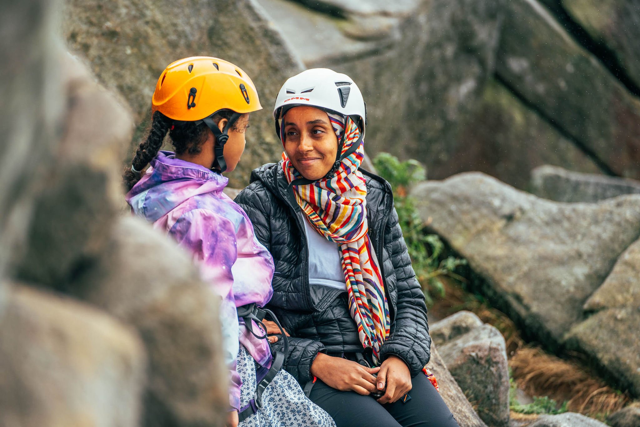 A woman looks at a child and smiles, they are both wearing climbing gear