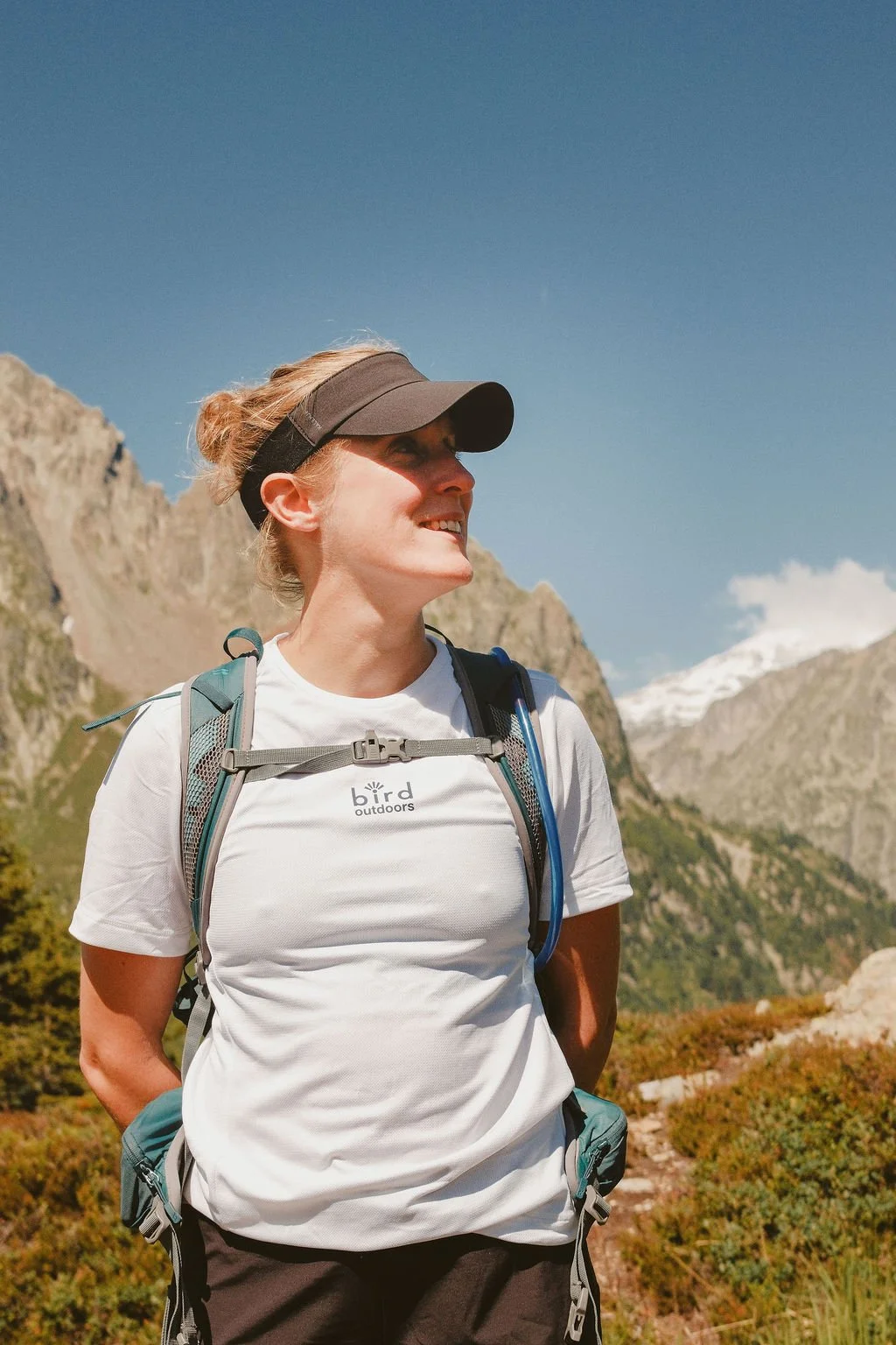 Elle is a white woman with light hair in this photo she looks to the right of the camera. she is in the mountains with a bird outdoors tshirt on.