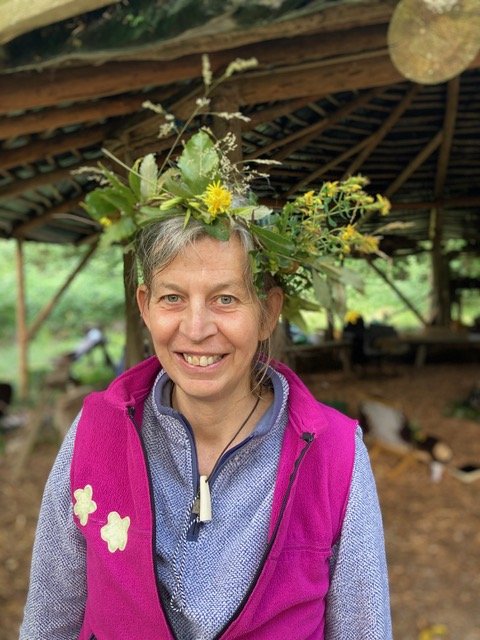 Jenny is an Apprentice-elder white woman; mid length greying hair, blue-green eyes. She wears a green headpiece made with foraged materials.