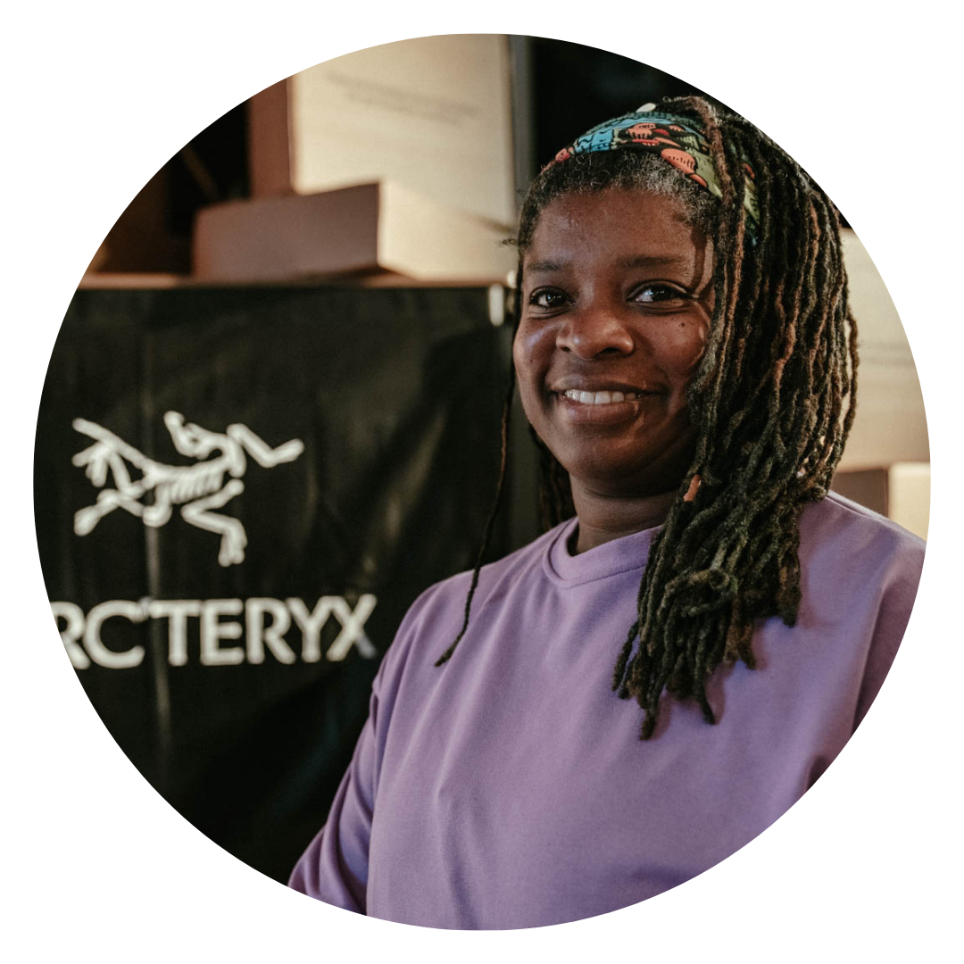 Marie is a  black woman, generous bodied with long matted locs, sometimes I wear glasses in this photo she wears a purple jumper and smiles to the camera.