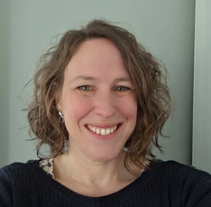 Leah is a white woman with short brown curly hair.