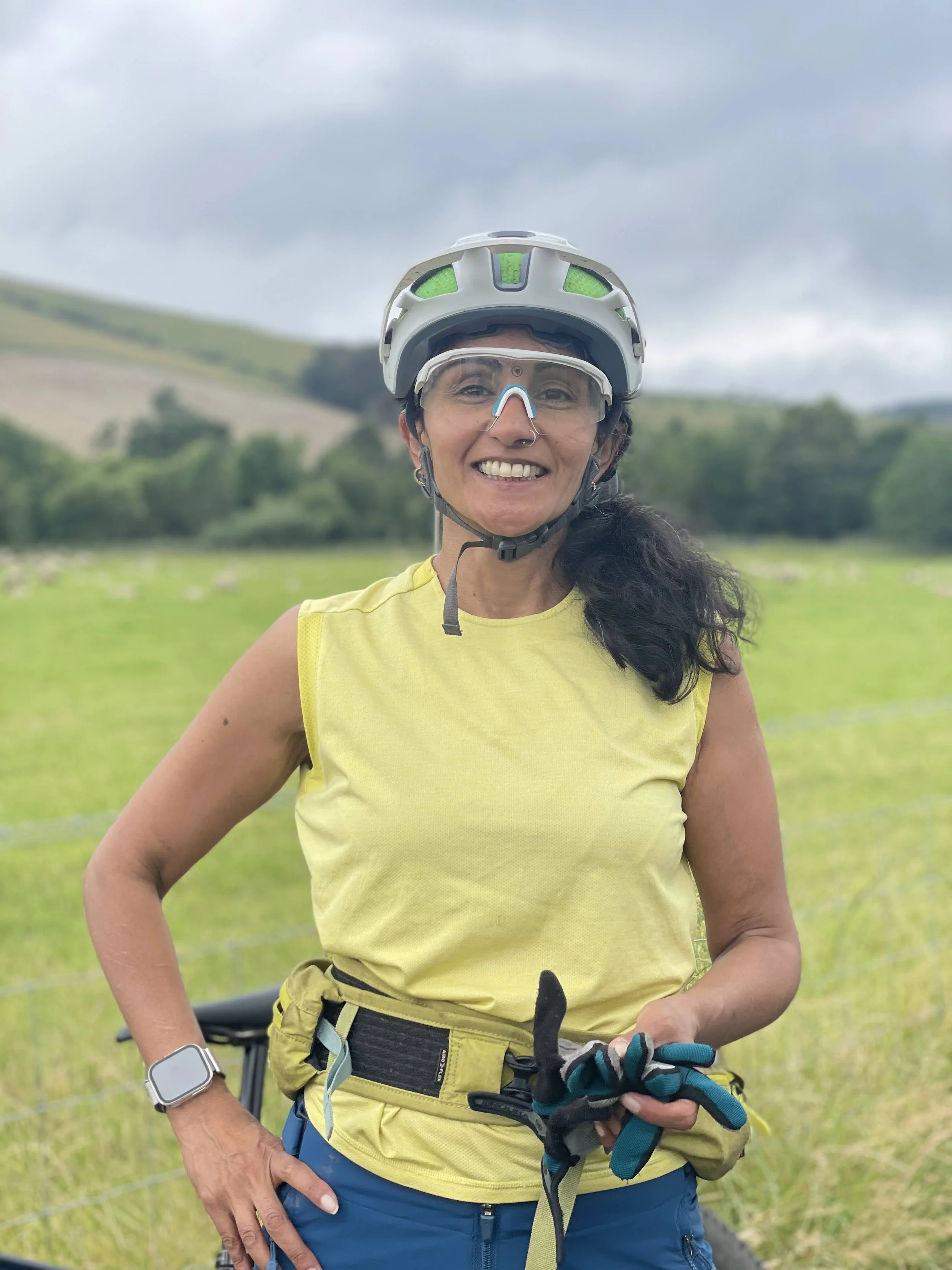 Aneela stands in a yellow top and cycling helmet smiling