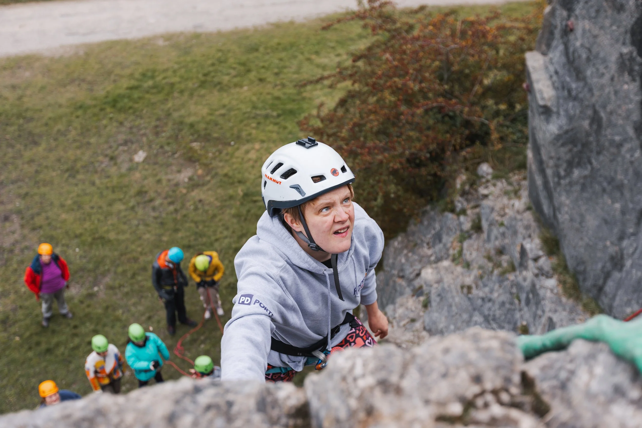 A top down photo of Pip as she climbs a grey rocky wall with people who look tiny below.