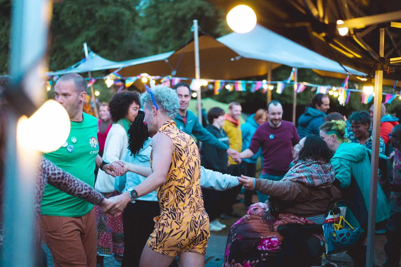 A group of people dance at ClimbOut Festival including AJ in an orange jumpsuit and blue horns, and a person in a wheelchair with a climbing helmet strapped to the back.