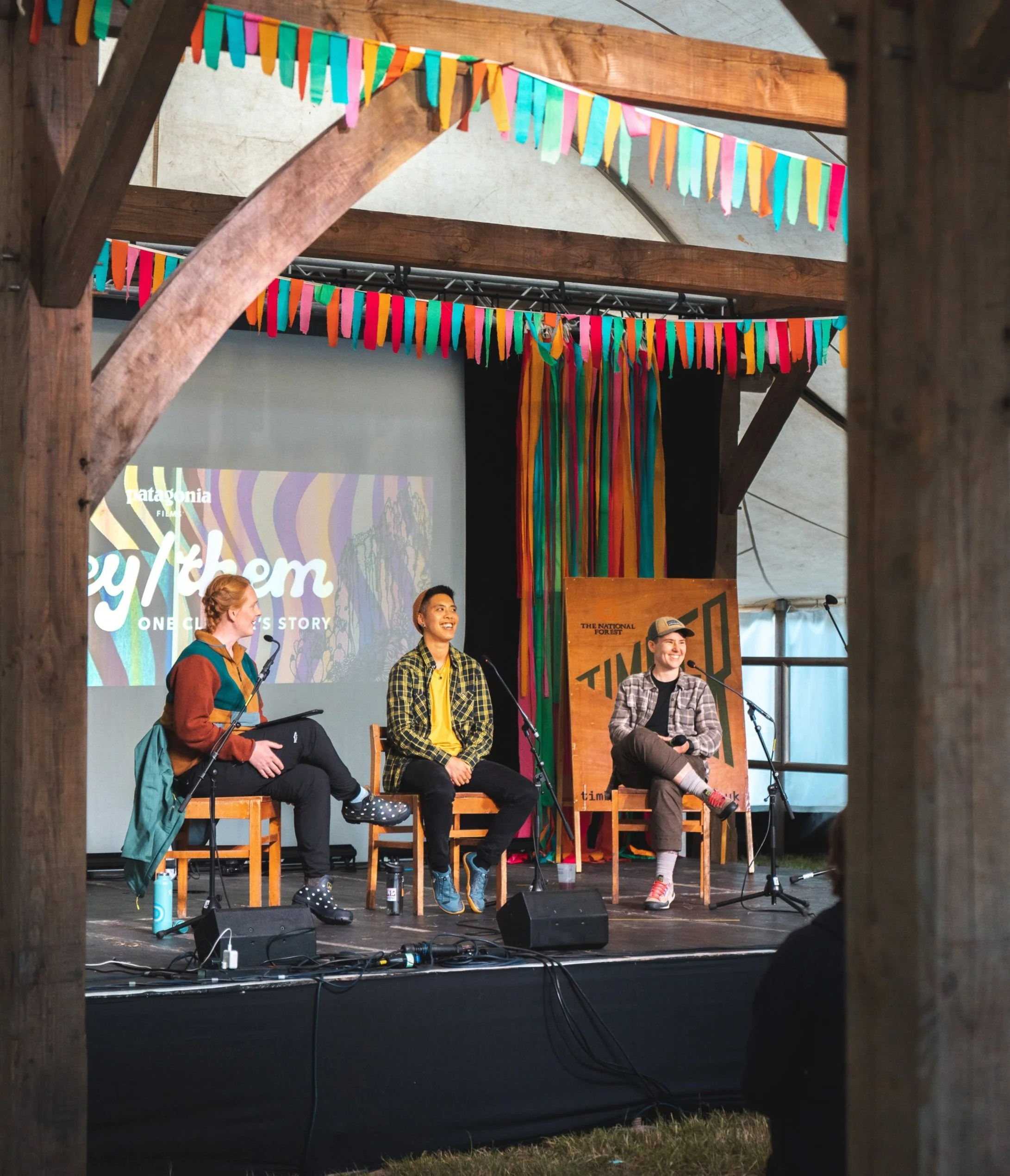 Eden, Frit and Simms on stage at Timber festival. They are all laughing and the stage is decorated with bunting.