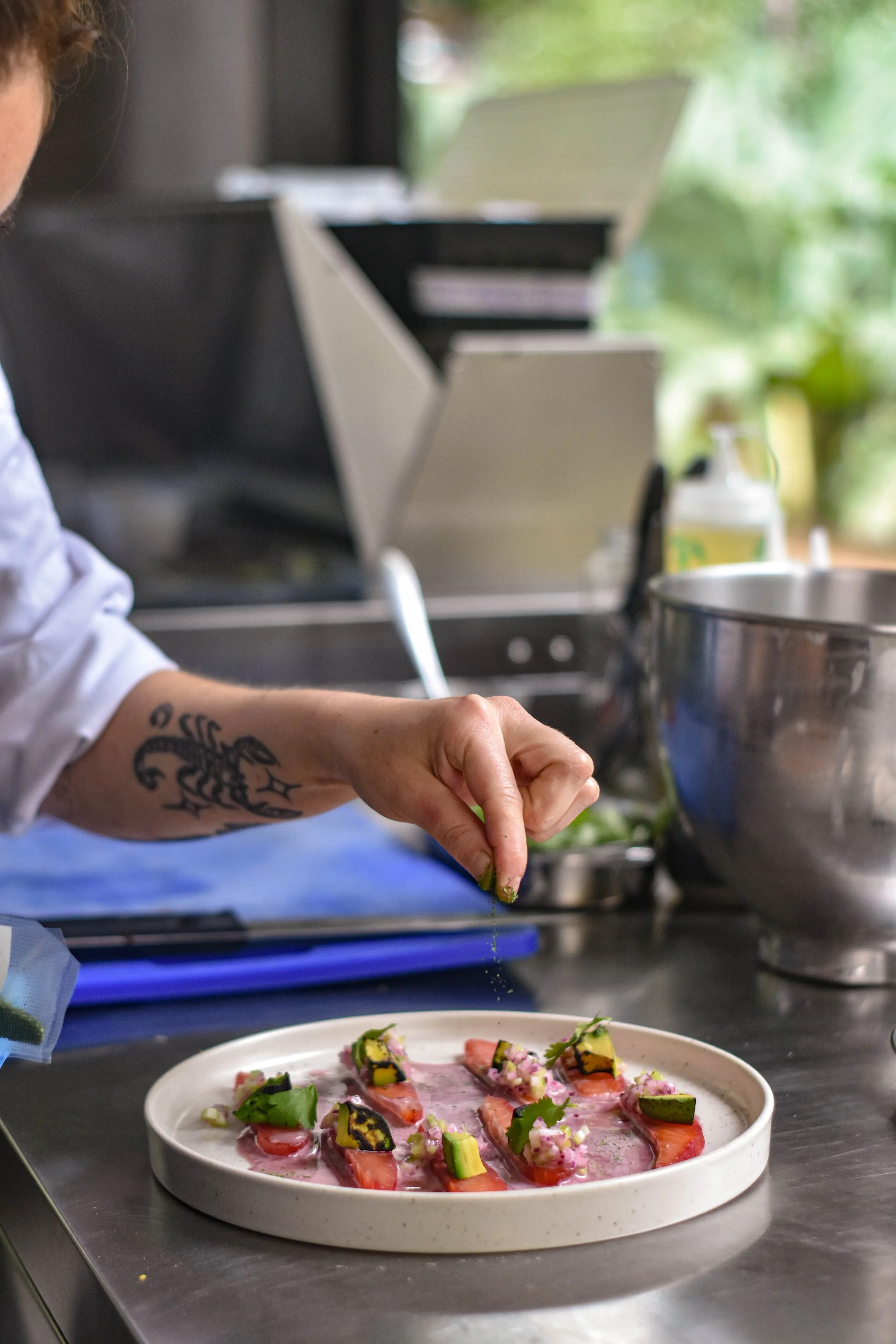 Persona decorando un plato con hierbas y vegetales en una cocina moderna.