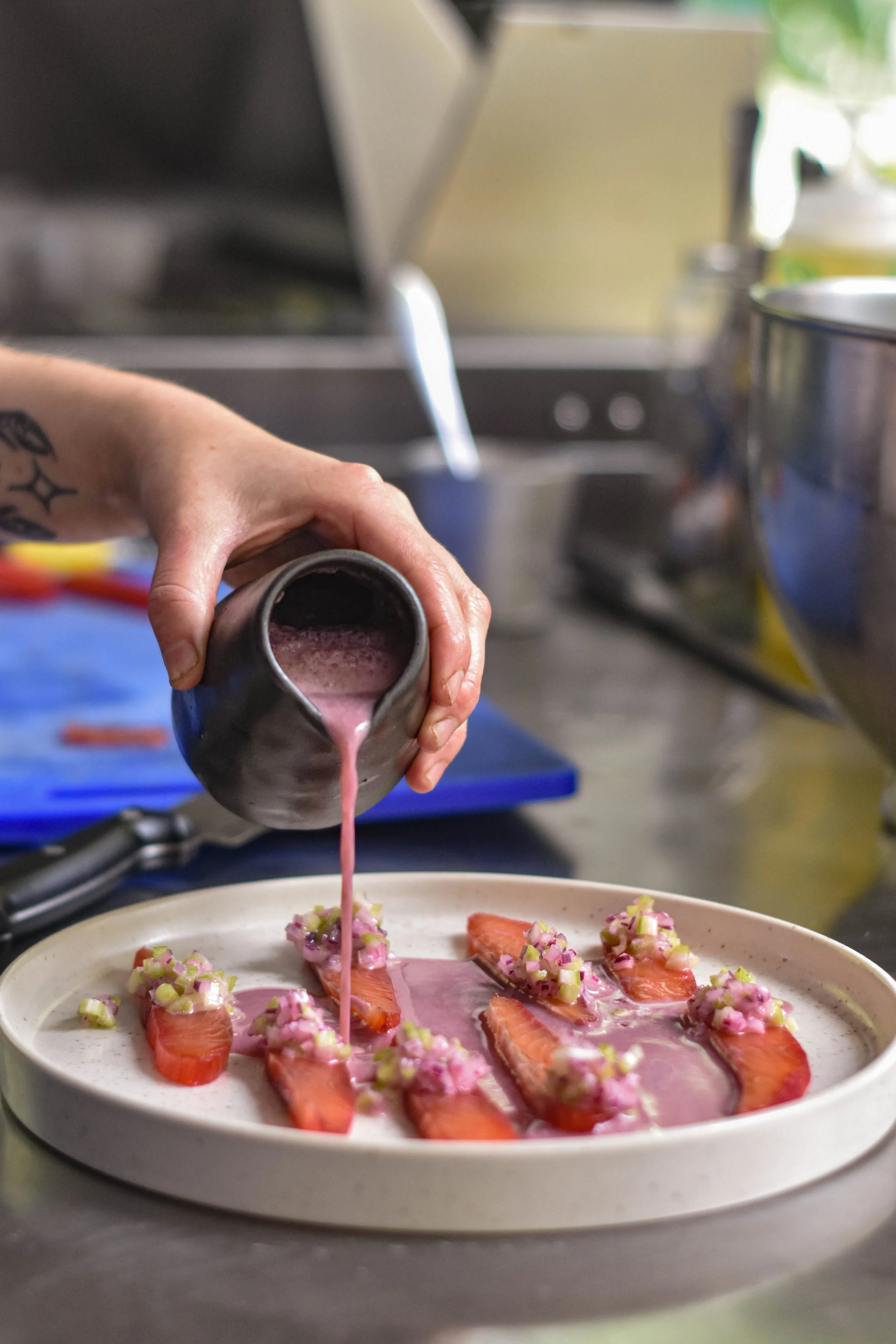 Una mano vierte una salsa rosada sobre un plato con fresas decoradas con cebolla y pimientos picados.