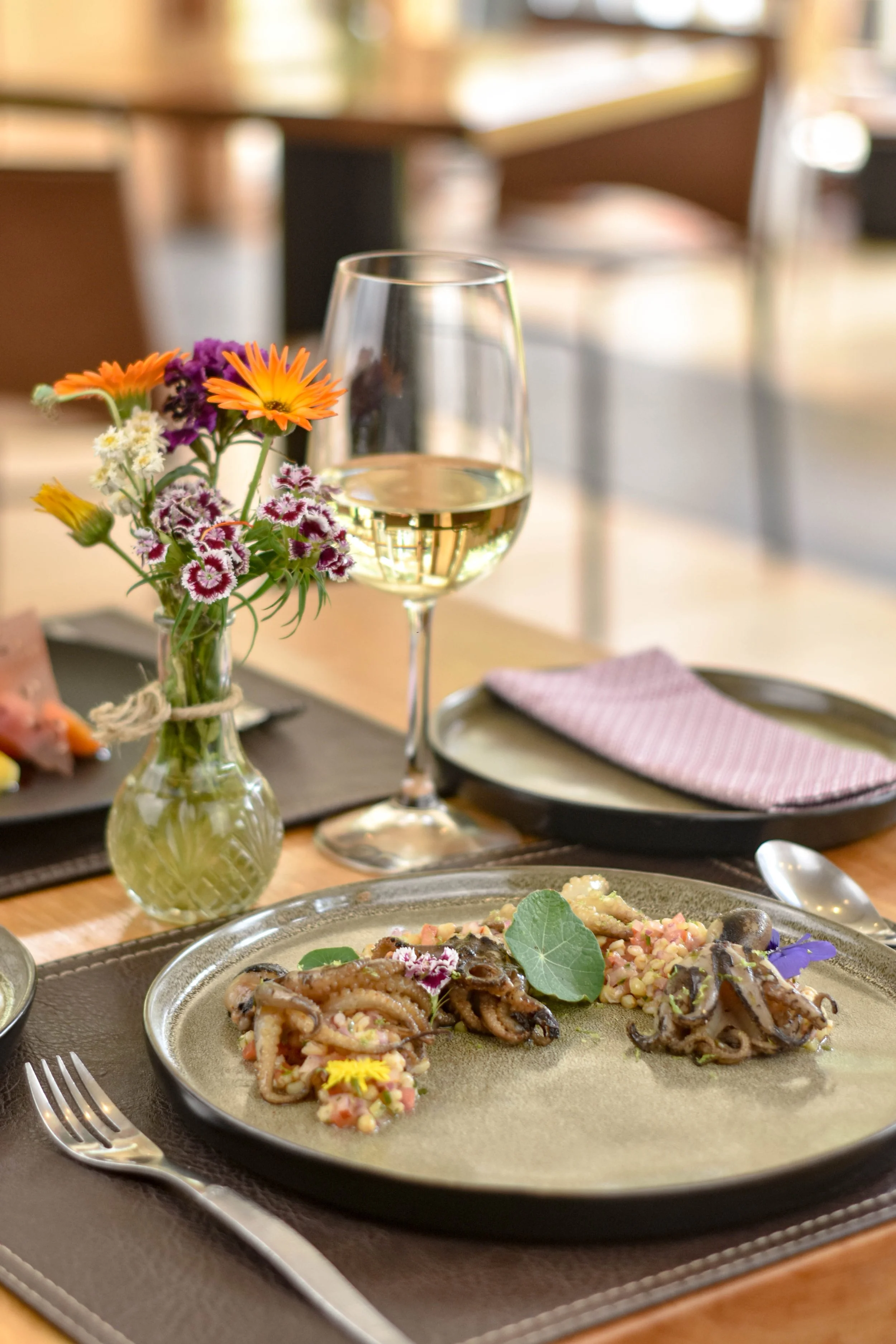 Plato de mariscos con vino blanco y un pequeño ramo de flores en un restaurante