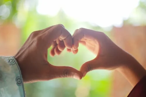 Hands forming a heart shape with the color green in the background representing Anahata