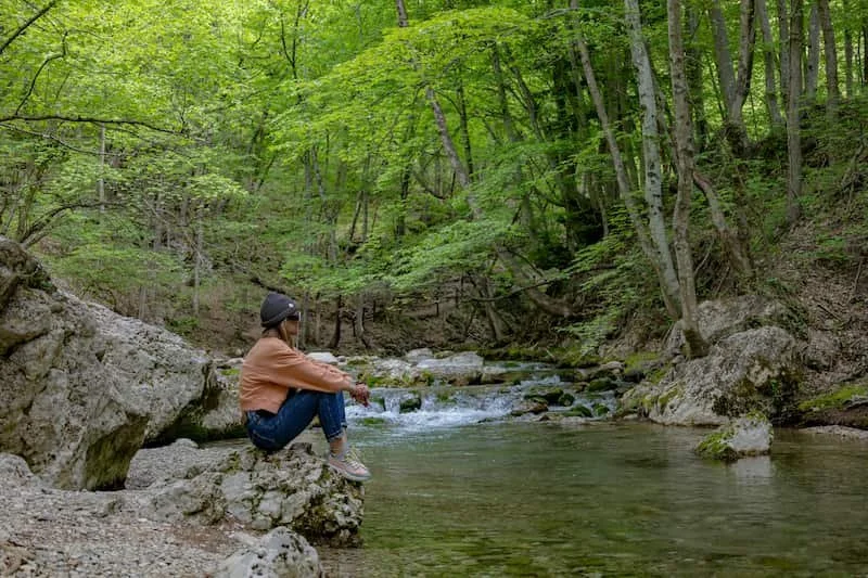 a woman sititng  in a forest by a river