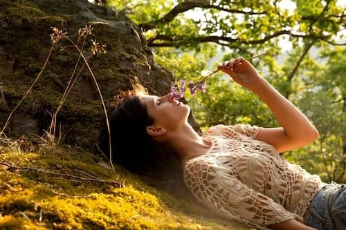 Woman relaxing and smelling a flower laying under a tree