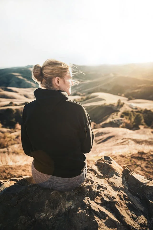 A woman sitting down on a rock on a hilltop