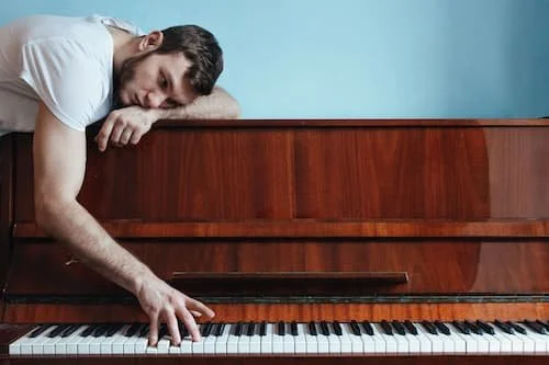 Man laying on top of piano looking sad and downtrodden