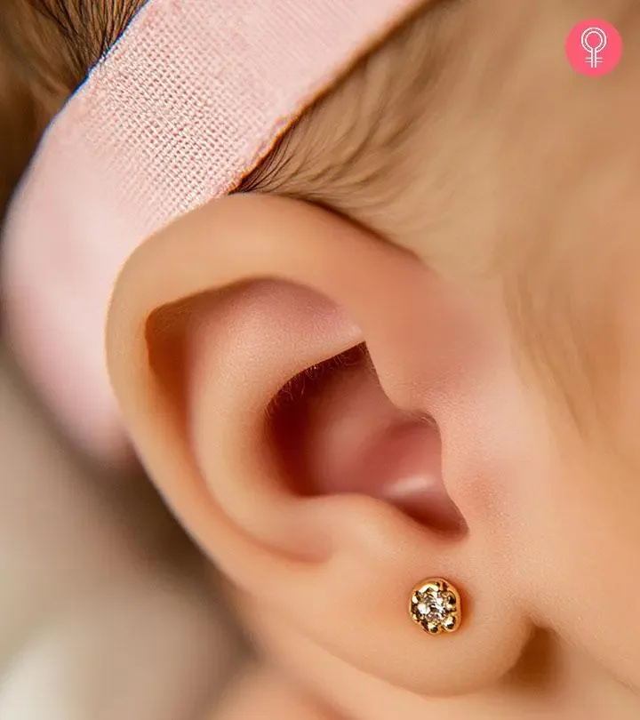 Close-up of a person's ear with a gold stud earring with multiple small diamonds. The person has a pink headband partially covering the hair.