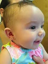 Close-up of a smiling baby girl with light skin and dark hair, wearing a colorful sleeveless top.