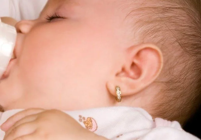 Close-up of a sleeping baby with a gold hoop earring in her ear, lying on a soft surface.