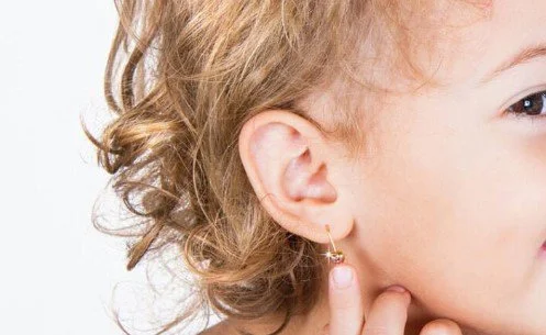 Close-up of a child's face, showing ear with a small hoop earring and curly hair, with the other eye and part of the face visible.
