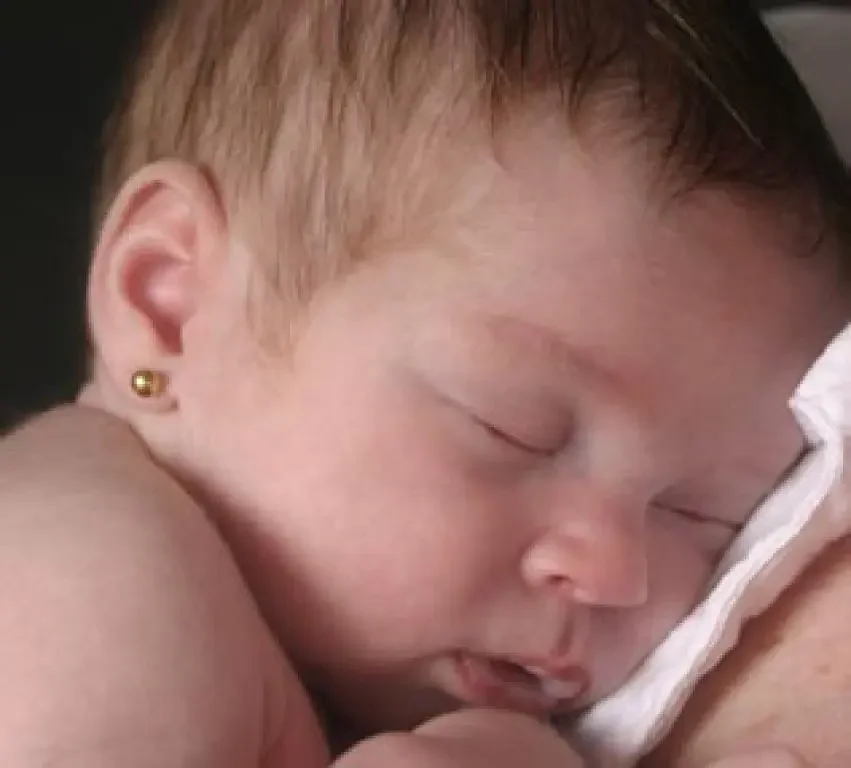 A close-up of a young person sleeping peacefully, lying on their side with a pillow, showing their face, ear with a small earring, and part of their shoulder.