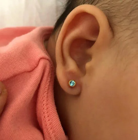 Close-up of a person's ear with a small, round, blue gemstone stud earring.