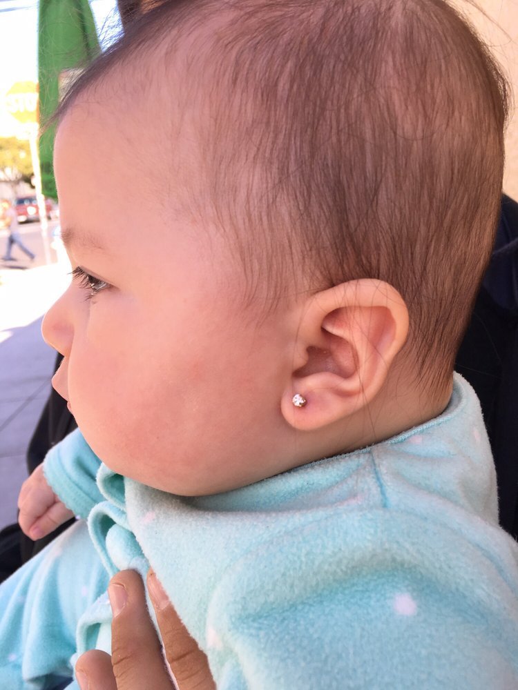 Close-up side view of a young child's head with a small diamond stud earring, wearing a light blue shirt, outdoors during daytime.