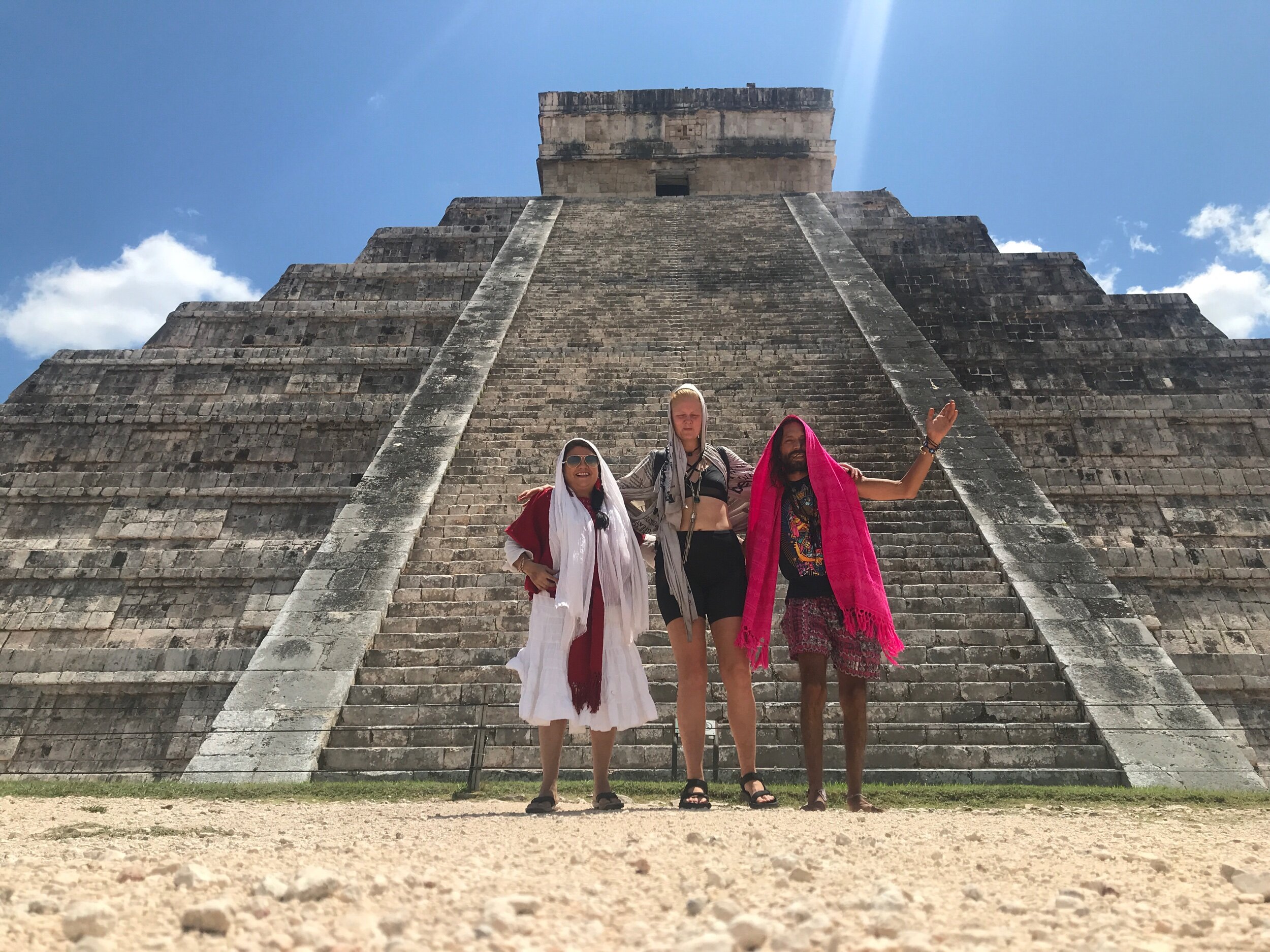 Three women standing in front of an ancient stepped pyramid at a Mayan archaeological site.