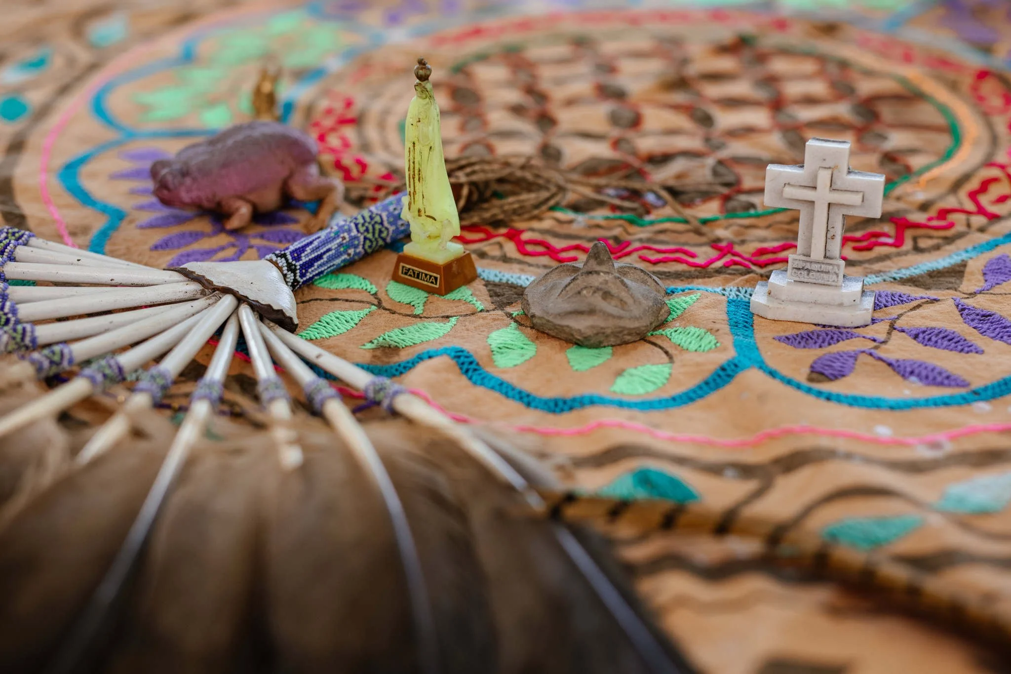 Colorful embroidered textile with small religious figurines, including a white cross and a yellow candle on a small stand, arranged on the altar for an ayahuasca ceremony.