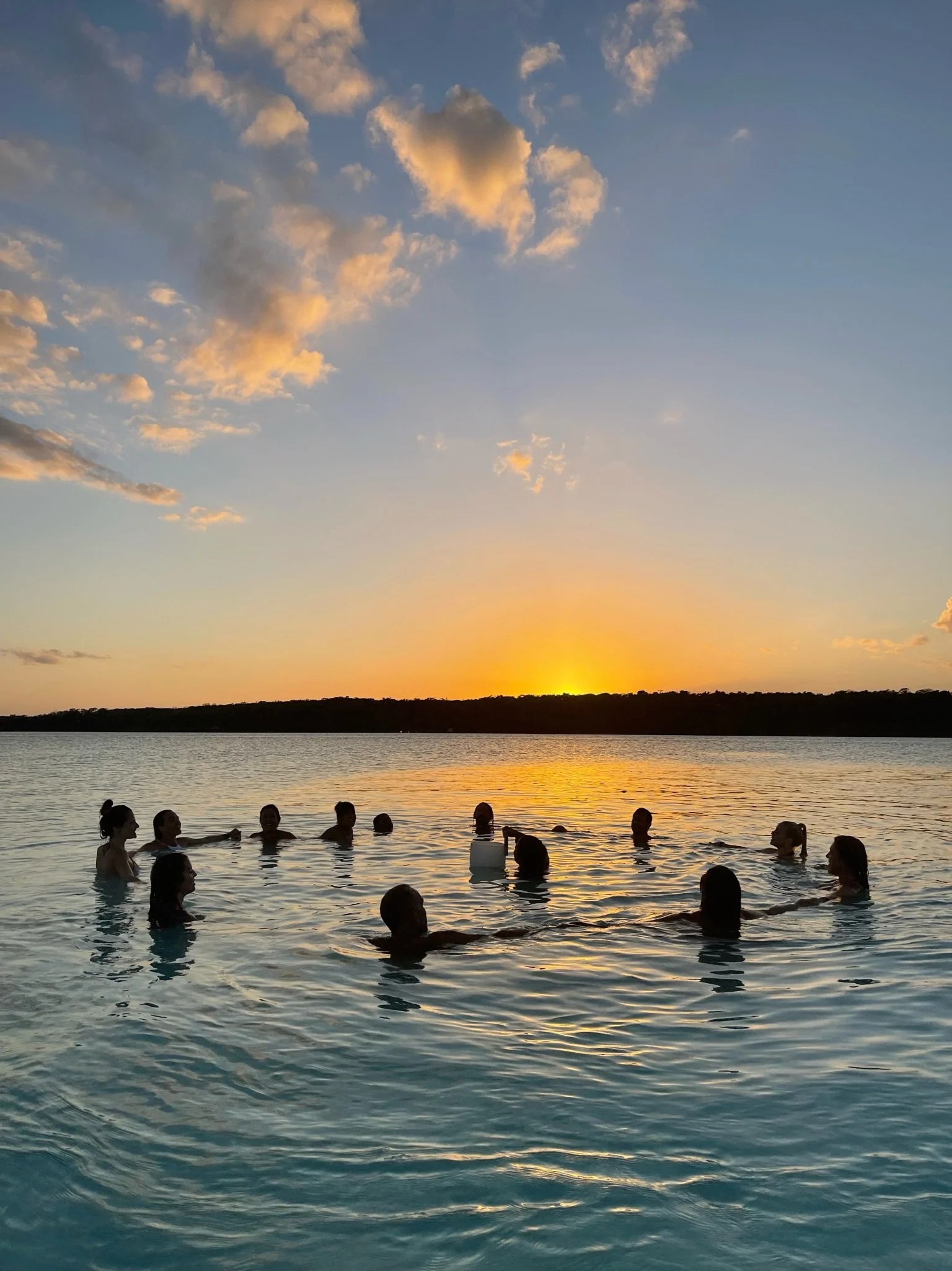 A group of people swimming in a lake during sunset with clouds in the sky.