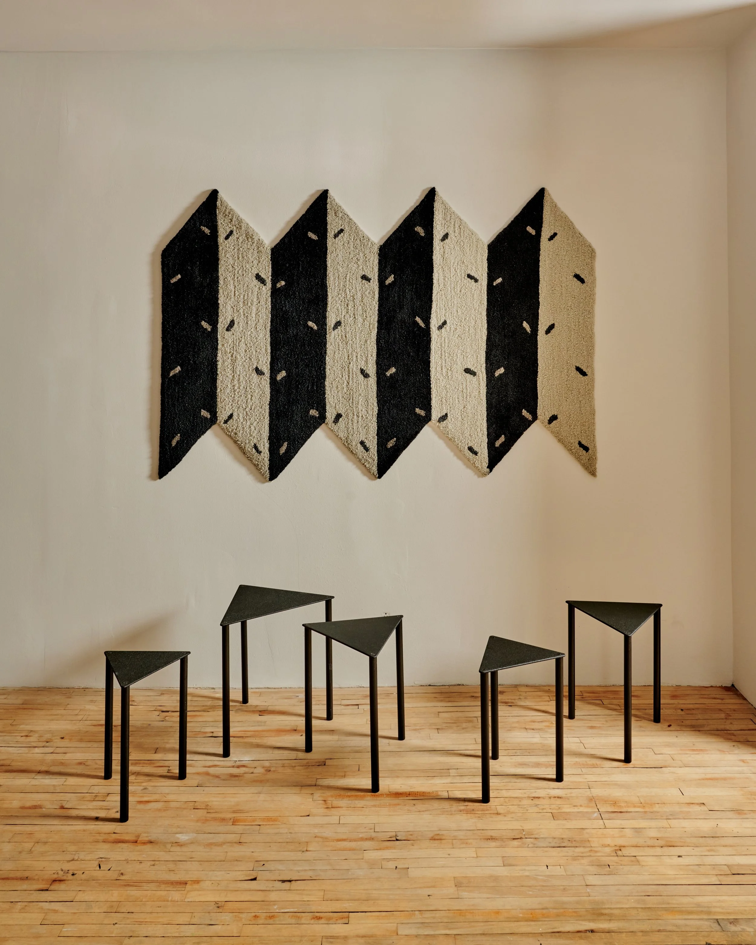 An interior room with a wooden floor, decorated with wall-mounted textile art and black tables.