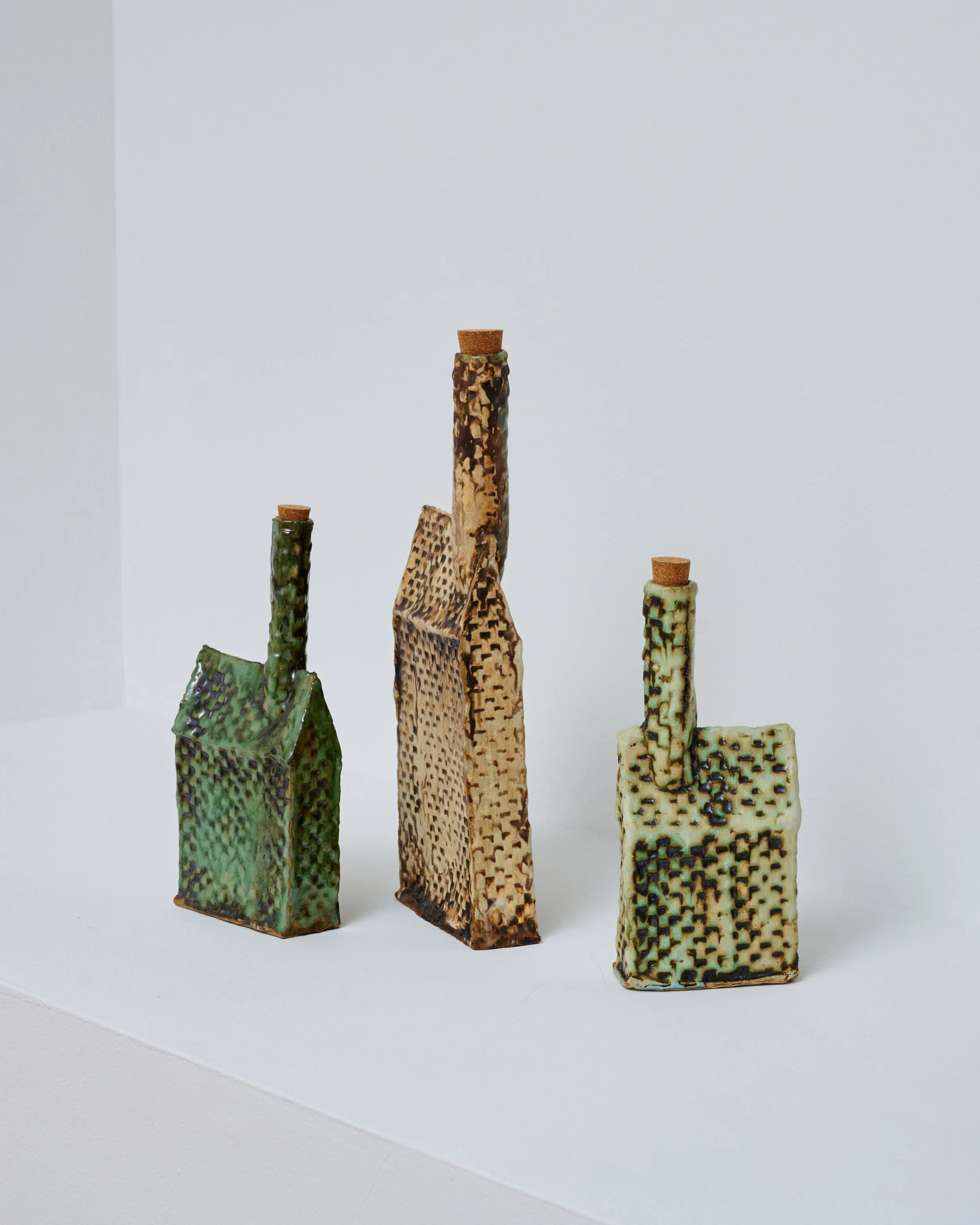 Ceramic sculptures resembling stylized buildings with chimney tops, varying in height and color, displayed on a white surface against a white background.