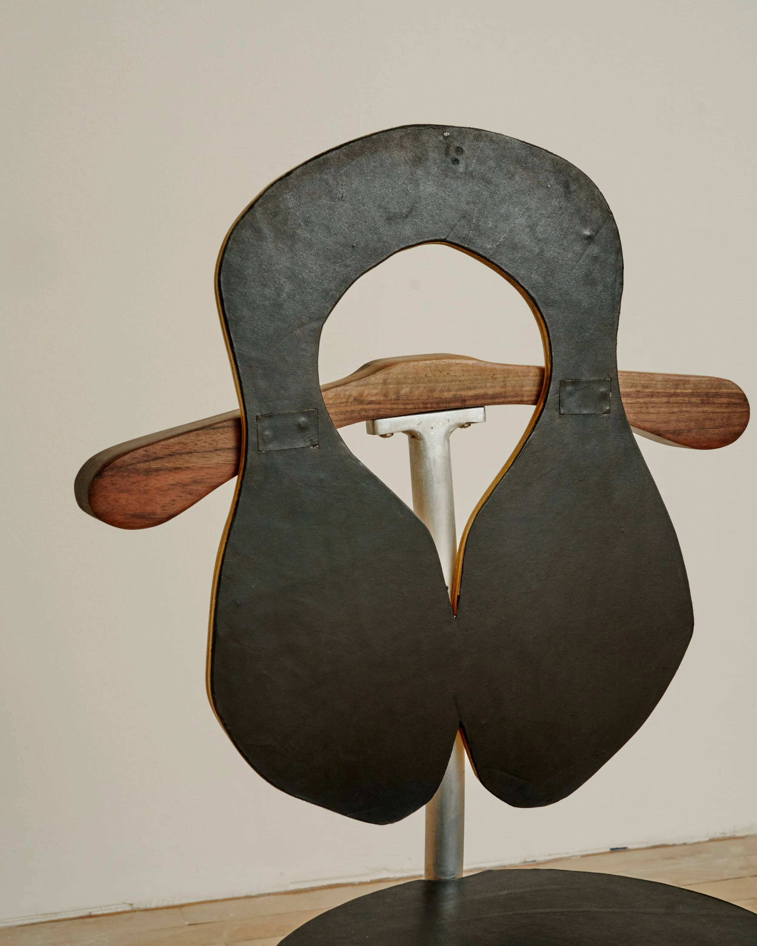 A sculpture resembling a black Macintosh computer icon with a slightly textured surface, mounted on a wooden stand with a metal pole, set against a plain white wall. Colin Knight.