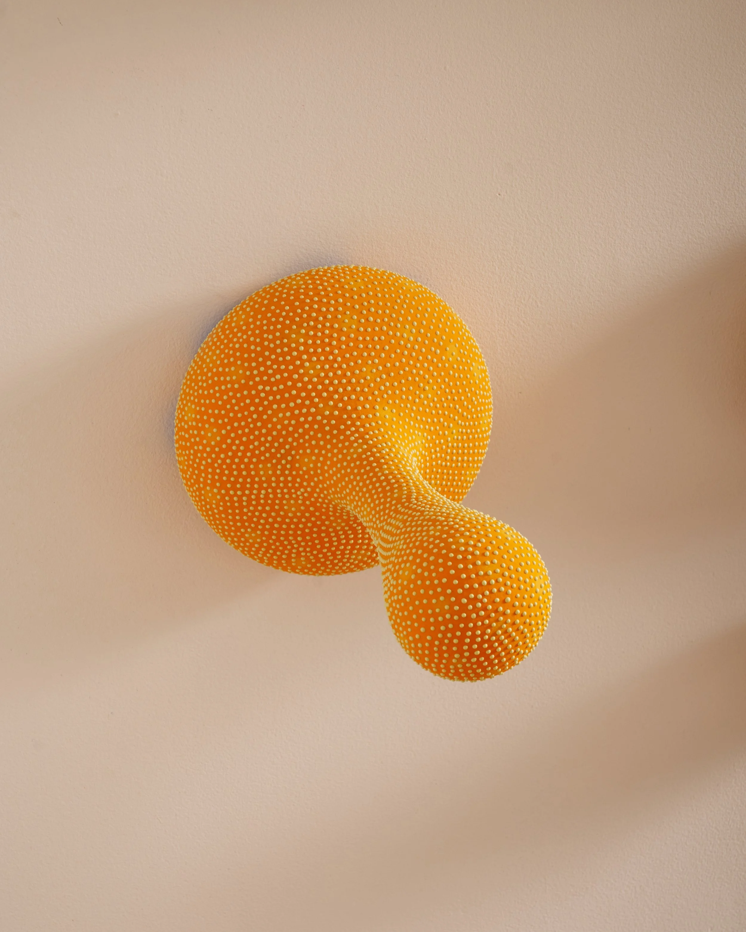 A yellow textured ball with small raised white dots on a plain beige surface. Joël Brodovsky-Adams.