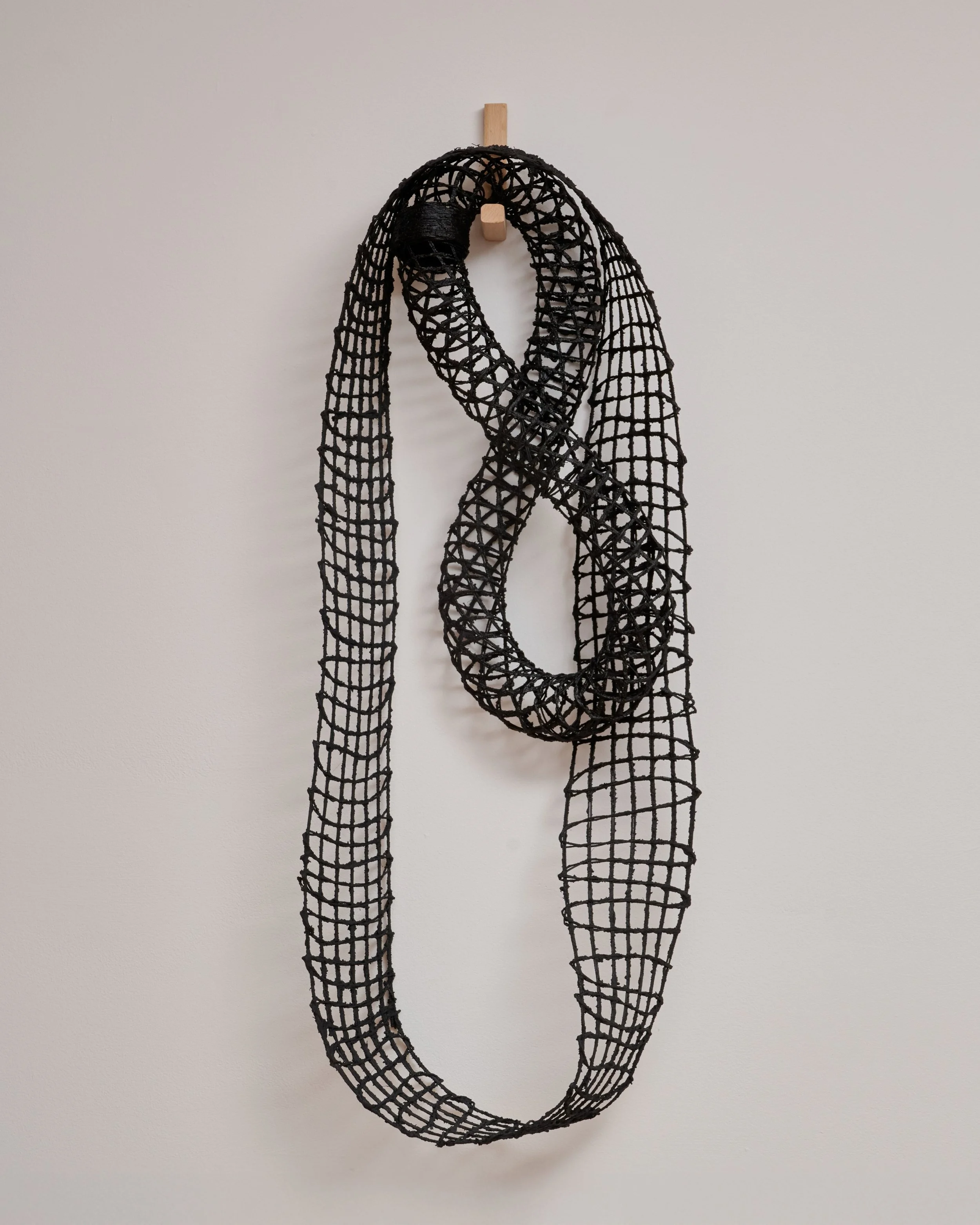 Black woven sculpture resembling a looped ribbon hanging on a wall.