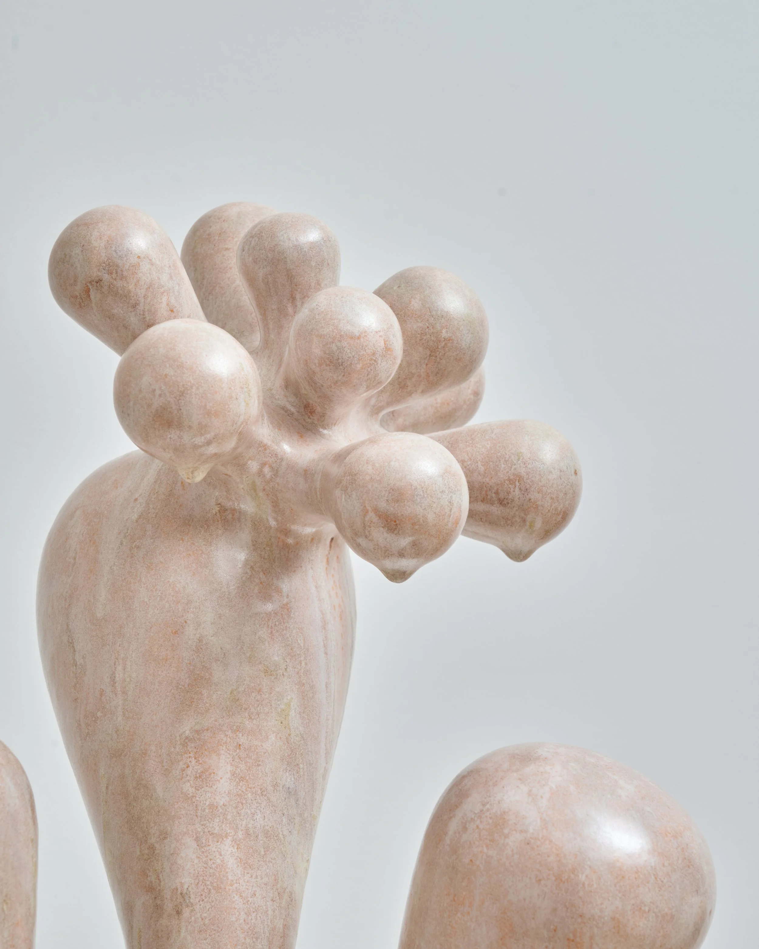 Close-up of a cluster of smooth, rounded, light-colored stones or ceramic objects with a matte finish against a plain white background. Joël Brodovsky-Adams.