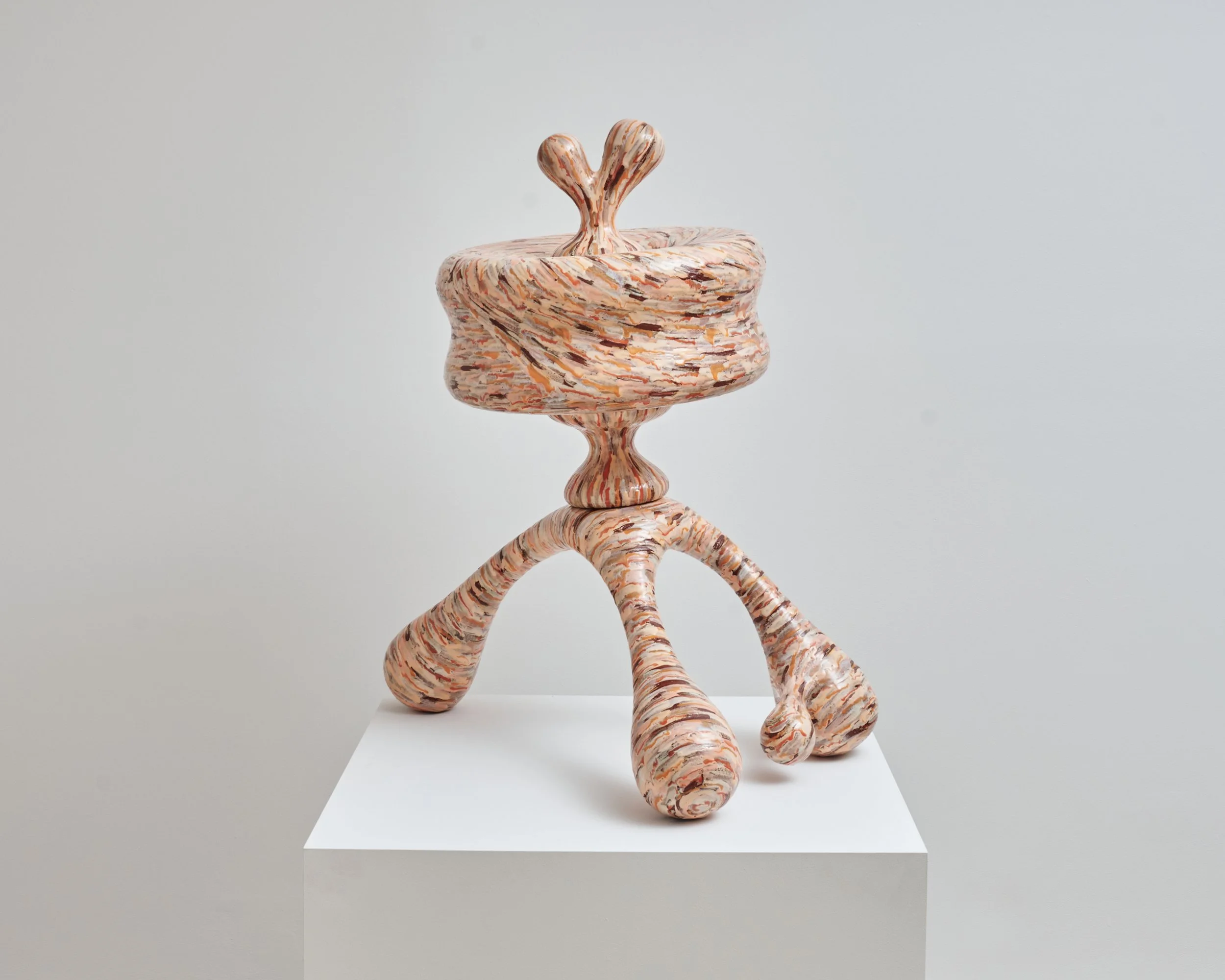 A modern sculpture made of layered, multicolored material resembling marble, shaped into a whimsical, abstract figure with a round, wide base, a slender neck, and two symmetrical, heart-shaped protrusions at the top. Joël Brodovsky-Adams.