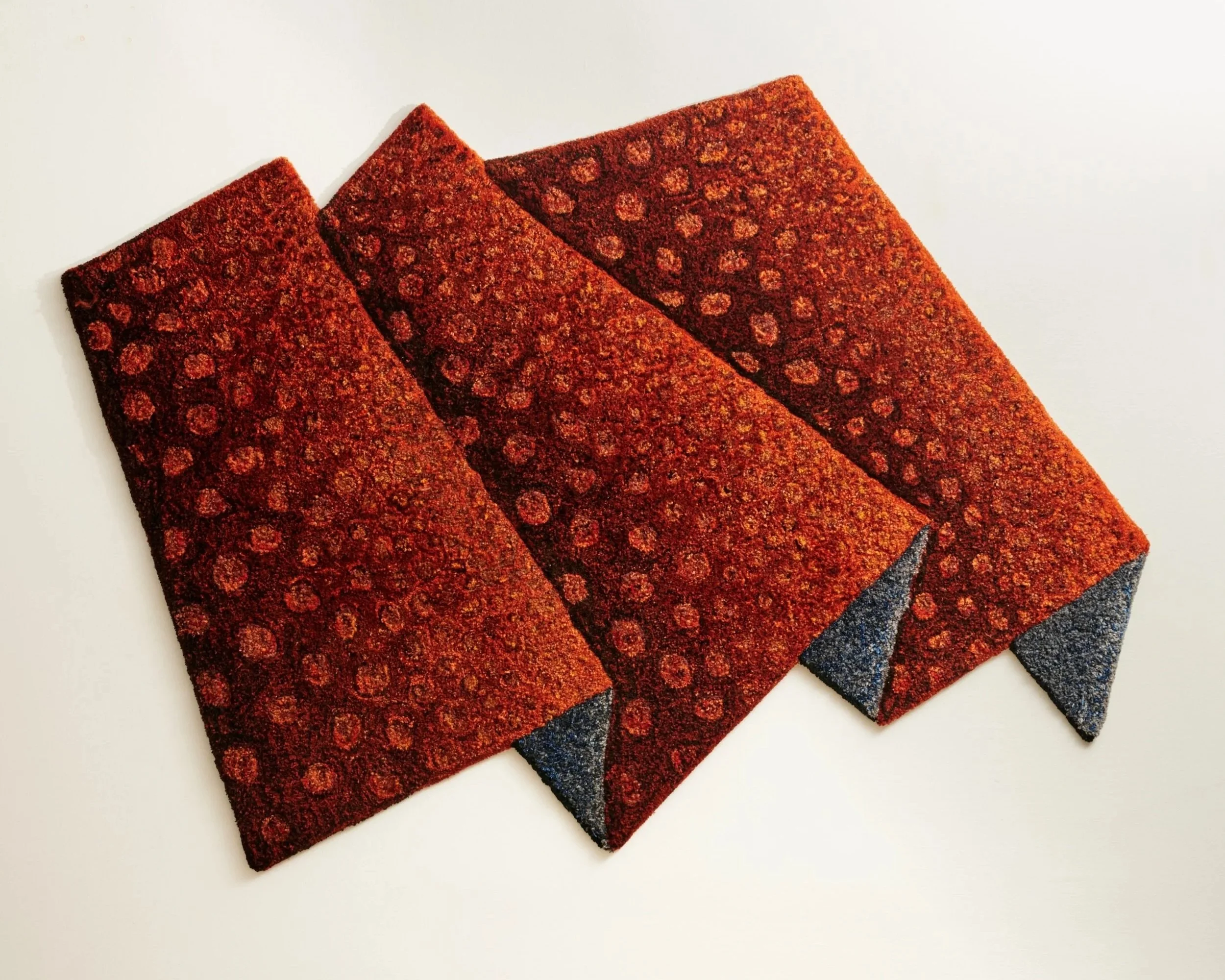 Three red and black textured welcome mats stacked on a white surface.